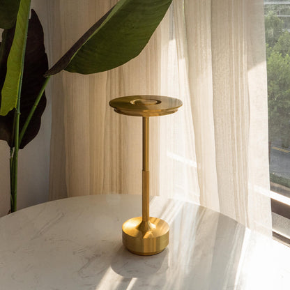 Gold side table on a marble surface with a plant and sheer curtains in the background