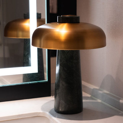 Gold table lamp with black base on a surface, reflecting in a mirror.