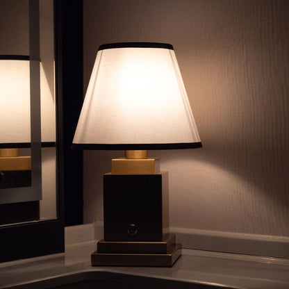Table lamp with a white shade and wooden base on a reflective surface.